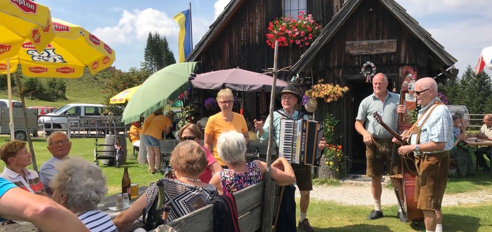 Eine Gruppe von Personen im Alter von 60+ auf einer Hütte, es wird musiziert und gesungen